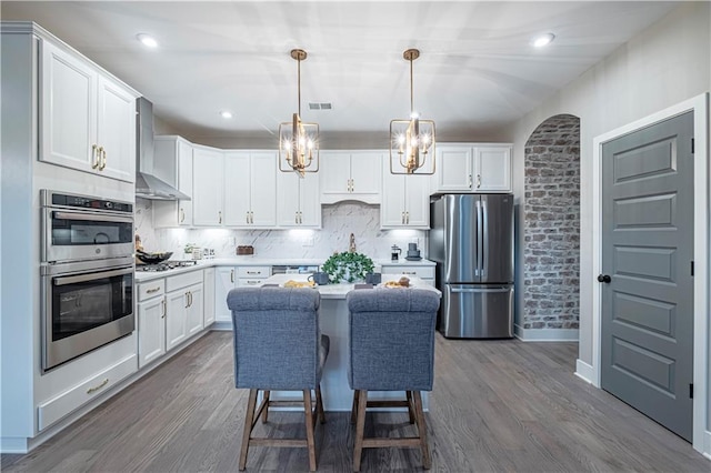 kitchen with hanging light fixtures, wall chimney range hood, stainless steel appliances, and white cabinetry