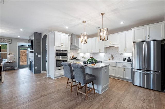 kitchen with white cabinets, wall chimney range hood, stainless steel appliances, and pendant lighting