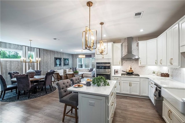 kitchen with white cabinetry, appliances with stainless steel finishes, decorative light fixtures, wall chimney exhaust hood, and a center island