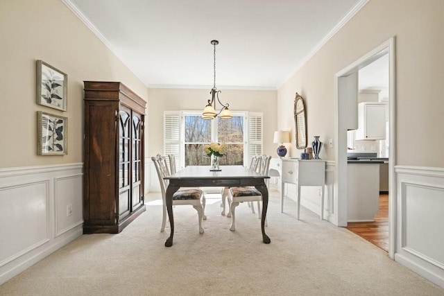 carpeted dining area with wainscoting, crown molding, and a decorative wall