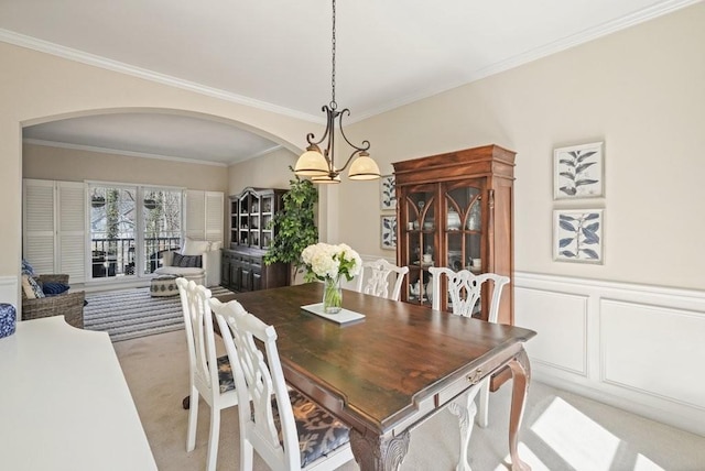 dining space featuring ornamental molding, wainscoting, a decorative wall, a notable chandelier, and light colored carpet