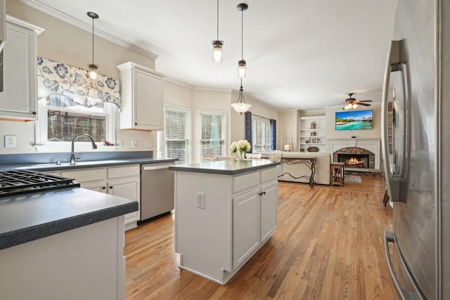 kitchen featuring dark countertops, a warm lit fireplace, stainless steel appliances, white cabinetry, and a sink