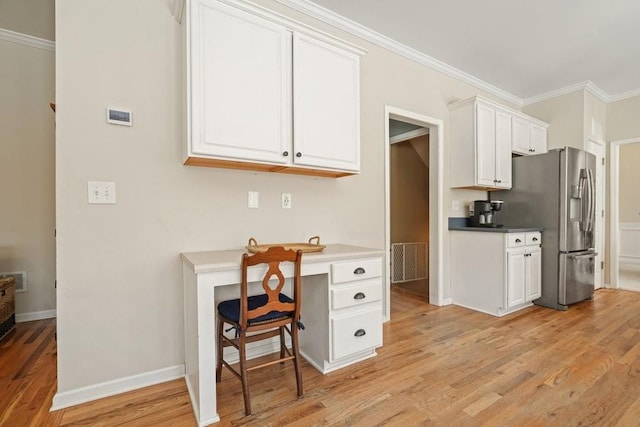 kitchen with light wood-style flooring, ornamental molding, stainless steel fridge, white cabinets, and baseboards