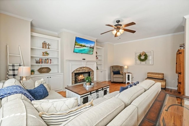 living area featuring wood finished floors, baseboards, ceiling fan, ornamental molding, and a lit fireplace