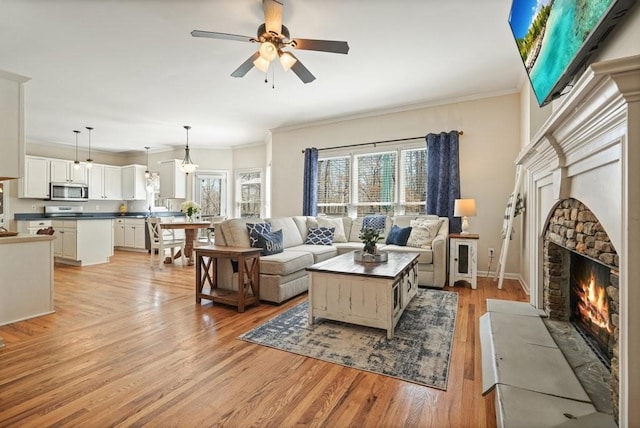 living room featuring a stone fireplace, a healthy amount of sunlight, crown molding, and light wood-style floors