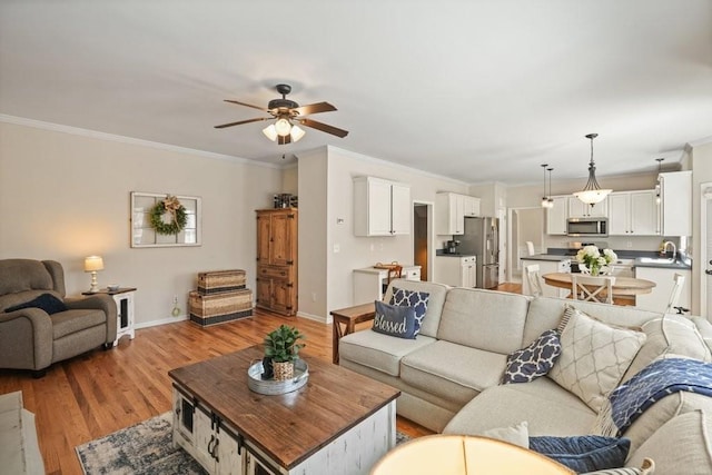 living area featuring baseboards, ornamental molding, and light wood finished floors