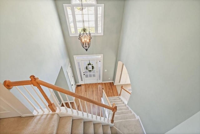 stairway featuring a high ceiling, a notable chandelier, wood finished floors, and baseboards