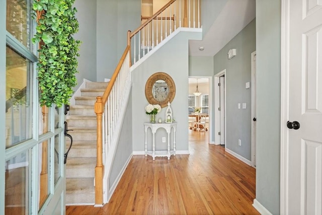 entryway with stairs, wood finished floors, baseboards, and a towering ceiling