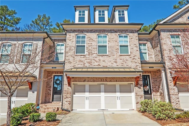 townhome / multi-family property featuring a standing seam roof, metal roof, brick siding, an attached garage, and concrete driveway