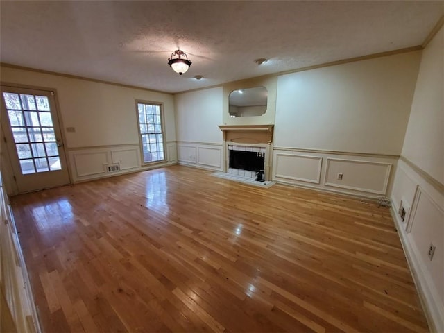542 Banks Rd E, Fayetteville, GA 30214 - unfurnished living room featuring a decorative wall, crown molding, a tiled fireplace, light wood-type flooring, and wainscoting