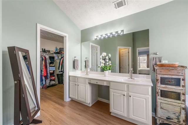 full bath featuring visible vents, double vanity, vaulted ceiling, wood finished floors, and a sink