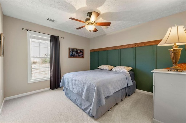 bedroom featuring visible vents, ceiling fan, baseboards, light carpet, and a textured ceiling