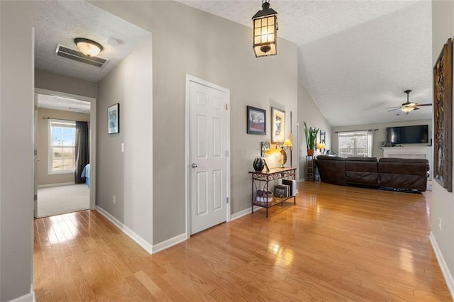 hallway with visible vents, lofted ceiling, light wood-style flooring, a textured ceiling, and baseboards