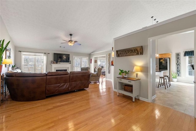 living area featuring ceiling fan, lofted ceiling, a fireplace, light wood-style floors, and a textured ceiling