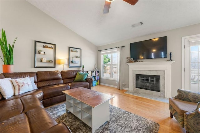 living area featuring vaulted ceiling, wood finished floors, a healthy amount of sunlight, and a premium fireplace