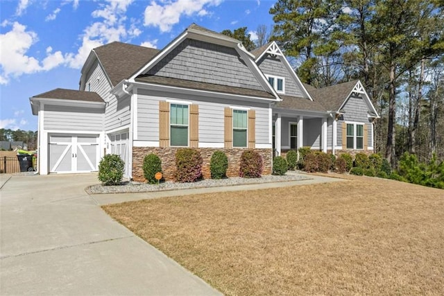 craftsman-style house with stone siding, a garage, a front lawn, driveway, and a shingled roof