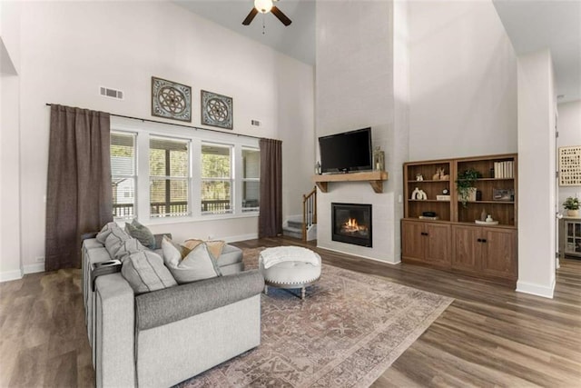 living area with a fireplace, wood finished floors, a towering ceiling, and a ceiling fan