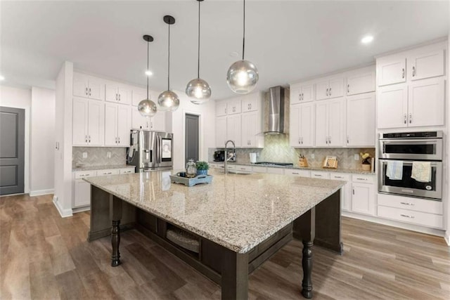 kitchen featuring white cabinetry, wall chimney exhaust hood, wood finished floors, a kitchen breakfast bar, and stainless steel appliances