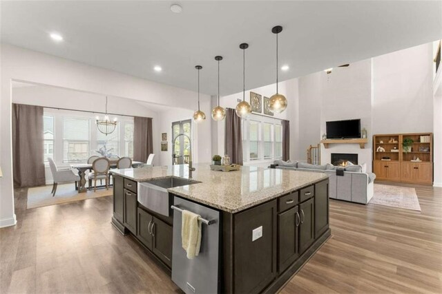 kitchen with a lit fireplace, a sink, light wood-type flooring, stainless steel dishwasher, and a notable chandelier