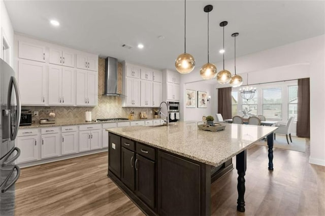 kitchen featuring white cabinetry, tasteful backsplash, a kitchen bar, stainless steel appliances, and wall chimney range hood