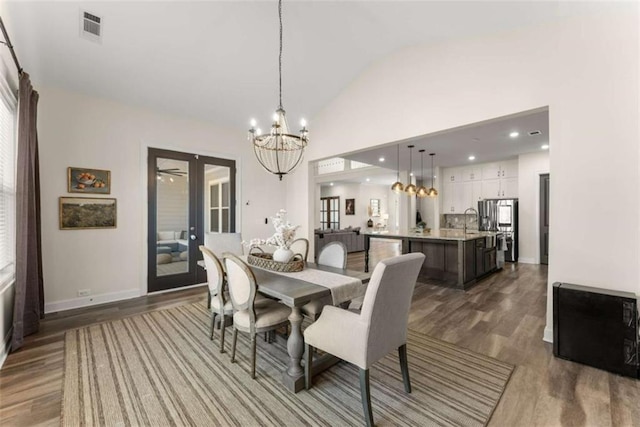 dining area featuring high vaulted ceiling, a chandelier, wood finished floors, baseboards, and visible vents