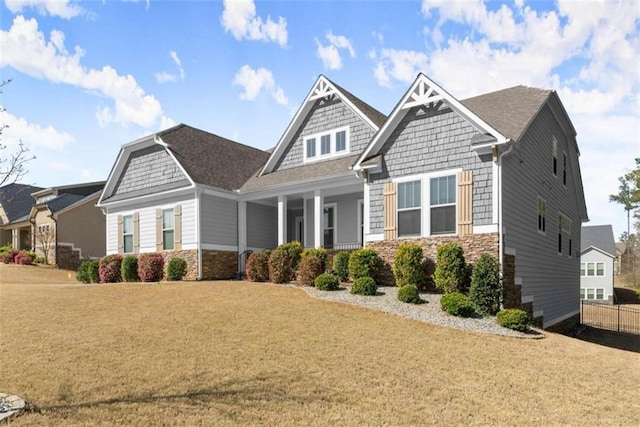 craftsman-style home with stone siding, fence, a front lawn, a shingled roof, and a porch