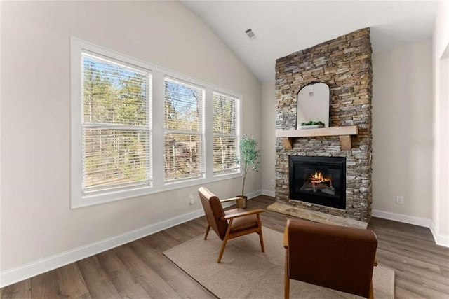 living area featuring a fireplace, visible vents, vaulted ceiling, and wood finished floors