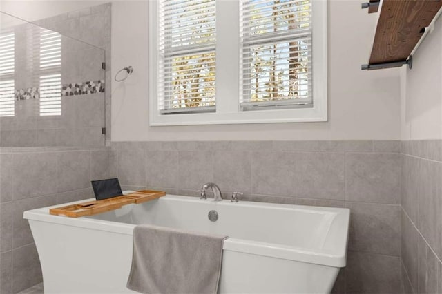 bathroom with tile walls, a wealth of natural light, and a freestanding bath