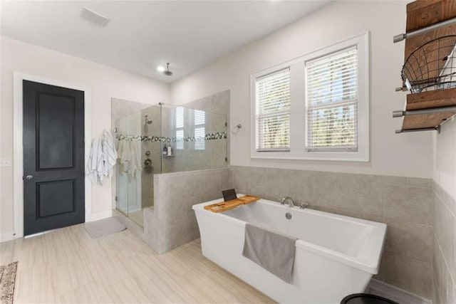 full bath with tile walls, a freestanding tub, and a shower stall