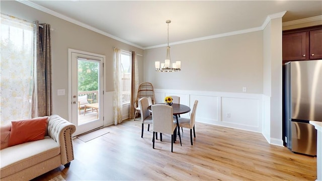 dining room featuring a wainscoted wall, ornamental molding, light wood-type flooring, and a notable chandelier