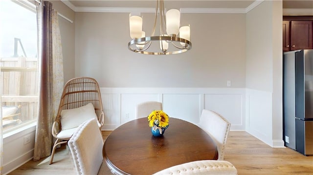 dining area with crown molding, a wainscoted wall, a notable chandelier, a decorative wall, and light wood-style flooring