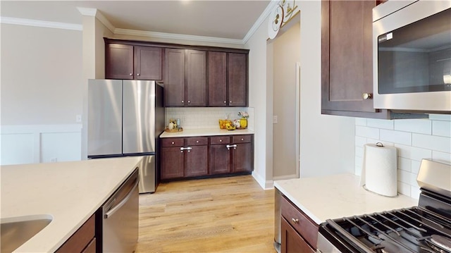 kitchen with light countertops, stainless steel appliances, ornamental molding, and light wood-style flooring