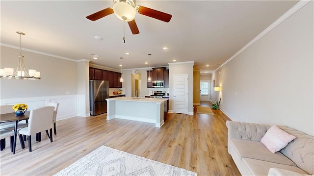 kitchen featuring appliances with stainless steel finishes, a sink, a center island with sink, open floor plan, and ornamental molding