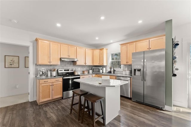 kitchen featuring a kitchen island, appliances with stainless steel finishes, a sink, under cabinet range hood, and backsplash