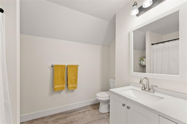 bathroom featuring toilet, wood finished floors, vanity, baseboards, and vaulted ceiling