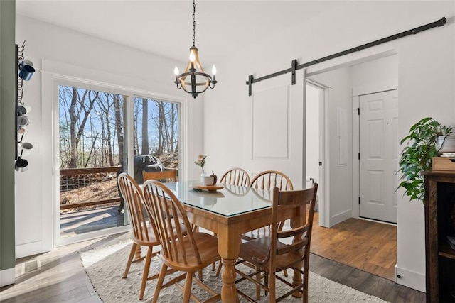 dining space featuring a barn door, wood finished floors, and an inviting chandelier