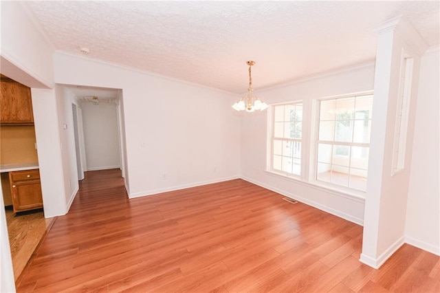 unfurnished dining area with ornamental molding, a textured ceiling, an inviting chandelier, light wood finished floors, and baseboards