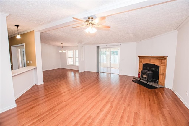 unfurnished living room featuring a textured ceiling, ceiling fan with notable chandelier, crown molding, a wood stove, and light wood-type flooring