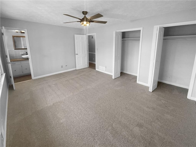 unfurnished bedroom featuring multiple closets, ceiling fan, ensuite bathroom, carpet floors, and a textured ceiling