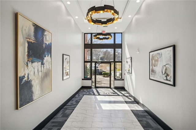 hallway featuring recessed lighting, a raised ceiling, a high ceiling, expansive windows, and baseboards