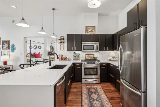 kitchen featuring stainless steel appliances, a peninsula, a sink, dark wood finished floors, and decorative light fixtures