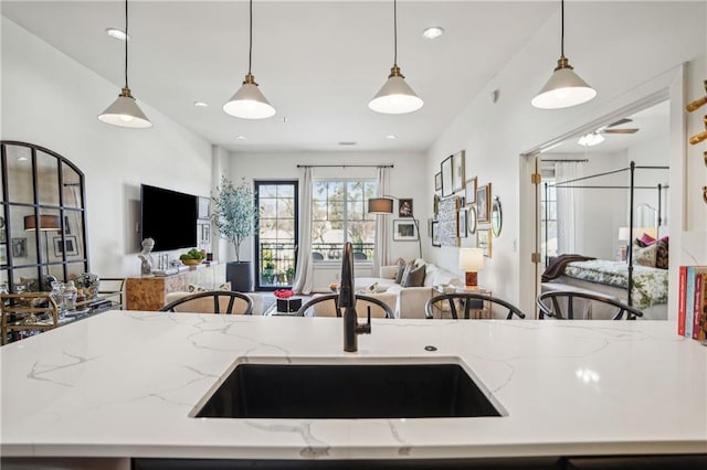 kitchen featuring open floor plan, light stone counters, a sink, and decorative light fixtures