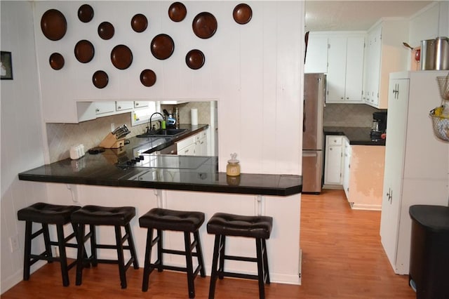 kitchen featuring a kitchen bar, white cabinets, stainless steel refrigerator, and kitchen peninsula