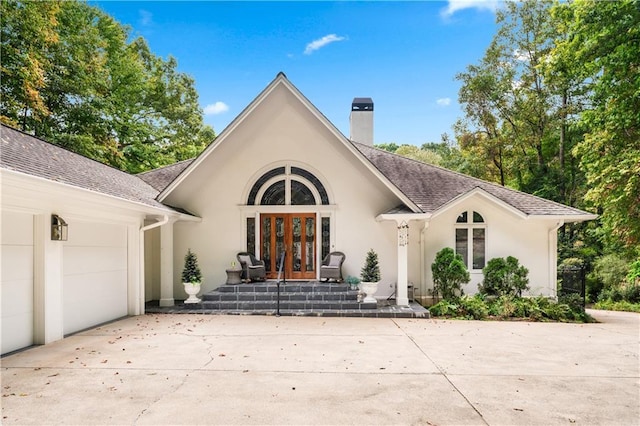 view of front of home with french doors, a chimney, stucco siding, concrete driveway, and a garage