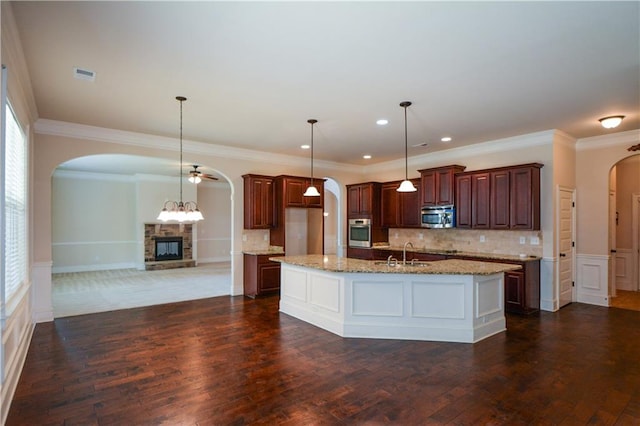 kitchen with appliances with stainless steel finishes, pendant lighting, light stone counters, and dark wood-type flooring