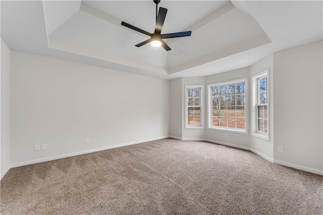 carpeted empty room featuring a tray ceiling, a ceiling fan, and baseboards