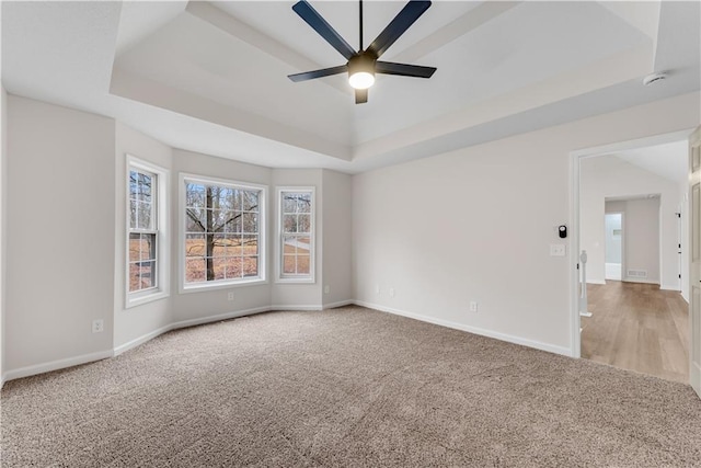 unfurnished room with a ceiling fan, carpet, a tray ceiling, and baseboards