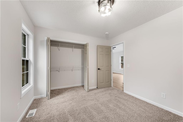 unfurnished bedroom with a textured ceiling, light carpet, visible vents, baseboards, and a closet