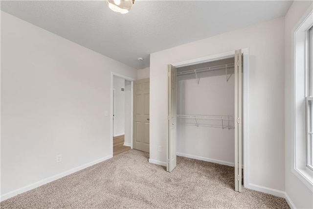 unfurnished bedroom with light carpet, a closet, a textured ceiling, and baseboards