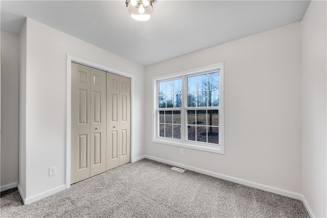 unfurnished bedroom with carpet floors, a closet, visible vents, a textured ceiling, and baseboards